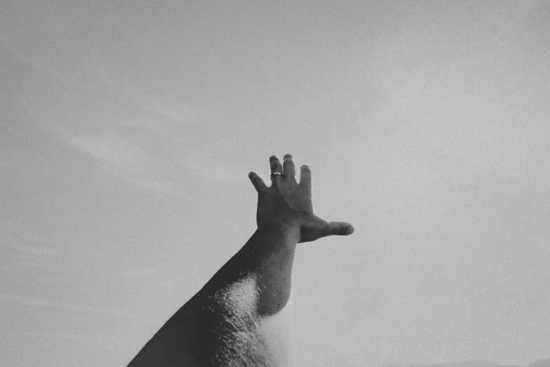 a black and white photo of a hand reaching up, by Carey Morris, pexels contest winner, surrealism, looking off into the distance, hot summer sun, [ floating ]!!, looking up at the camera