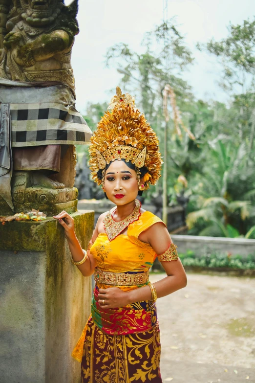 a woman in a yellow dress standing next to a statue, pexels contest winner, sumatraism, ornate headdress, square, : :, outside