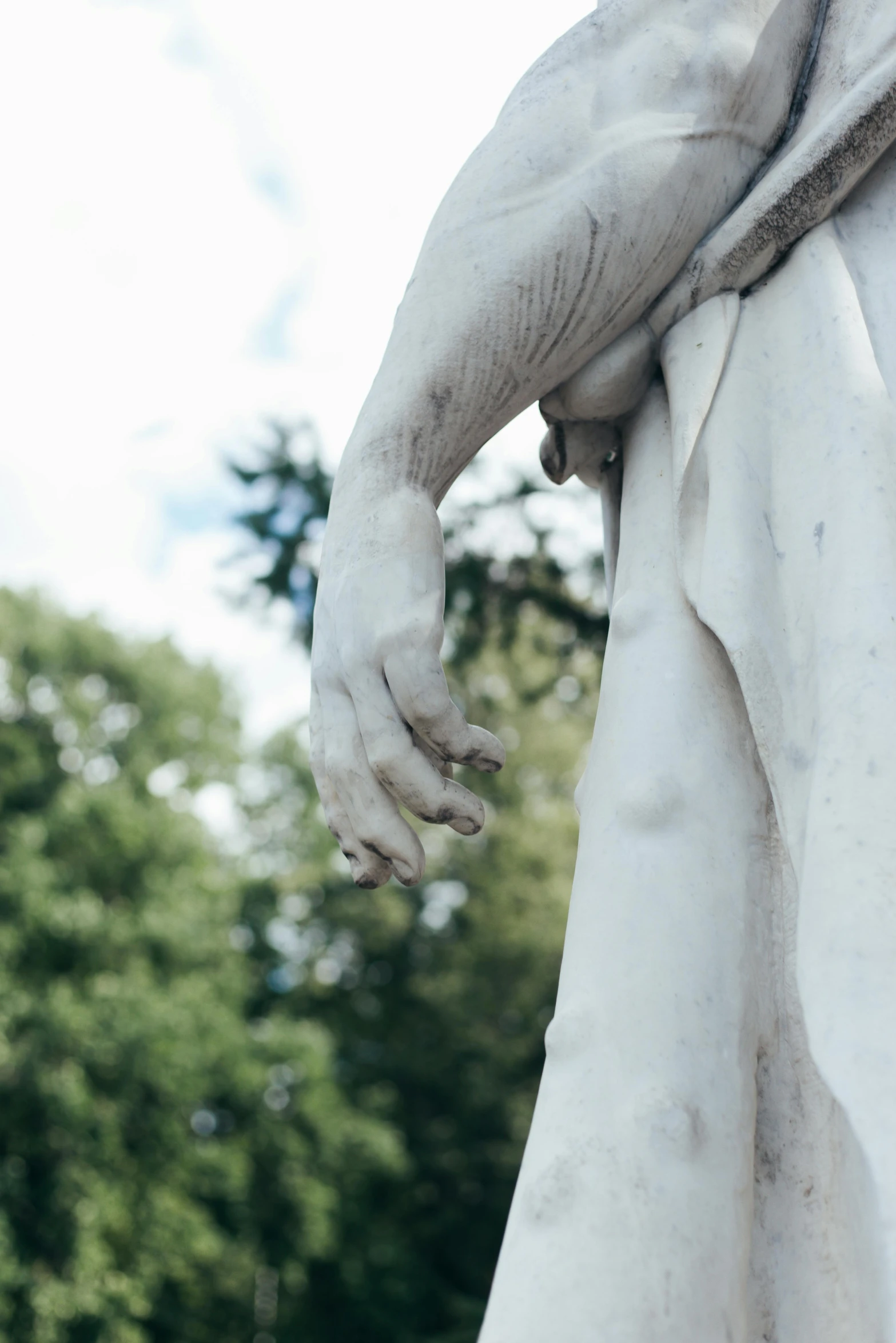 a close up of a statue with trees in the background, by Niko Henrichon, unsplash, close-up of thin soft hand, arched back, cementary, white sleeves