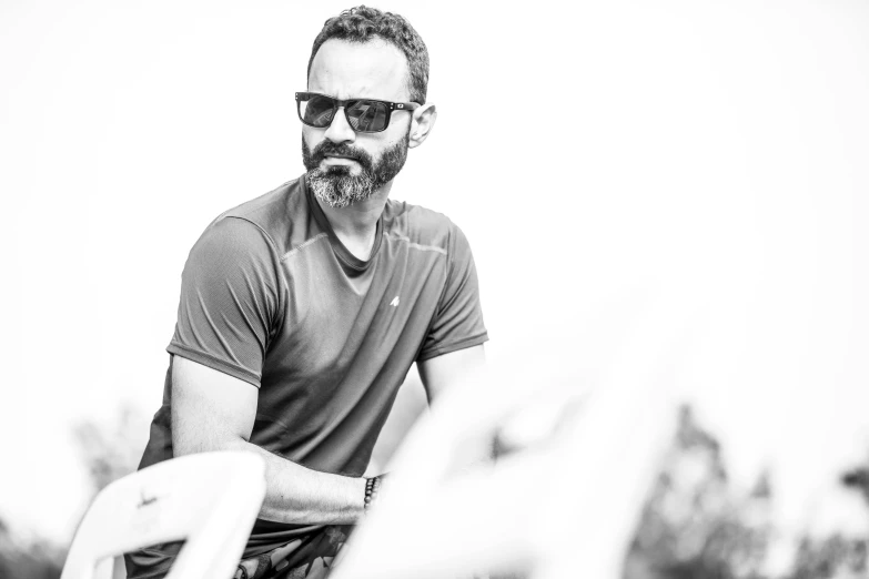 a man that is sitting down with a frisbee, by Giorgio Cavallon, wearing oakley sunglasses, black curly beard, portait photo profile picture, man in his 40s