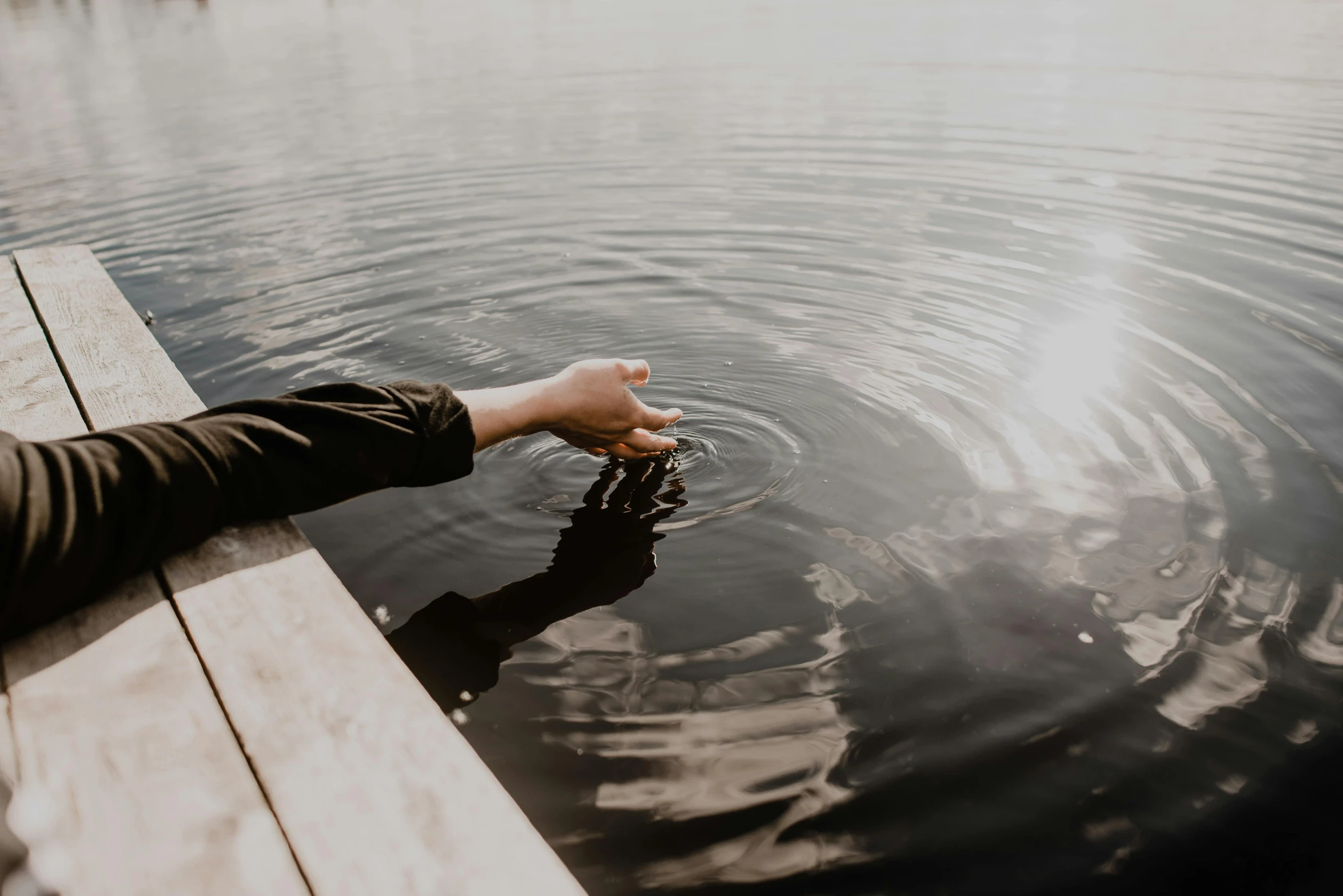 a person standing on a dock next to a body of water, by Emma Andijewska, pexels contest winner, happening, two hands reaching for a fish, water ripples, subtle detailing, floating drowned