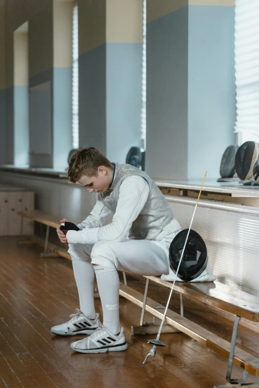 a man sitting on a bench using a cell phone, fencer, looking sad, profile image, sports setting