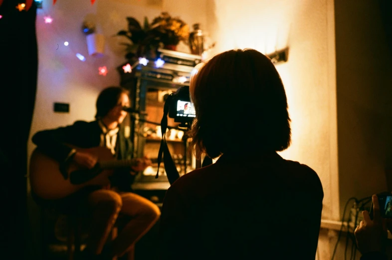 a woman taking a picture of a man playing a guitar, inspired by Nan Goldin, pexels contest winner, visual art, home video footage, profile image, tiny person watching, ( ( theatrical ) )