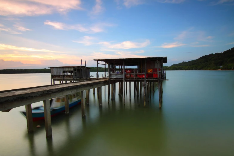 a boat sitting on top of a lake next to a pier, by Basuki Abdullah, pexels contest winner, hurufiyya, houses on stilts, al fresco, youtube thumbnail, serene colors