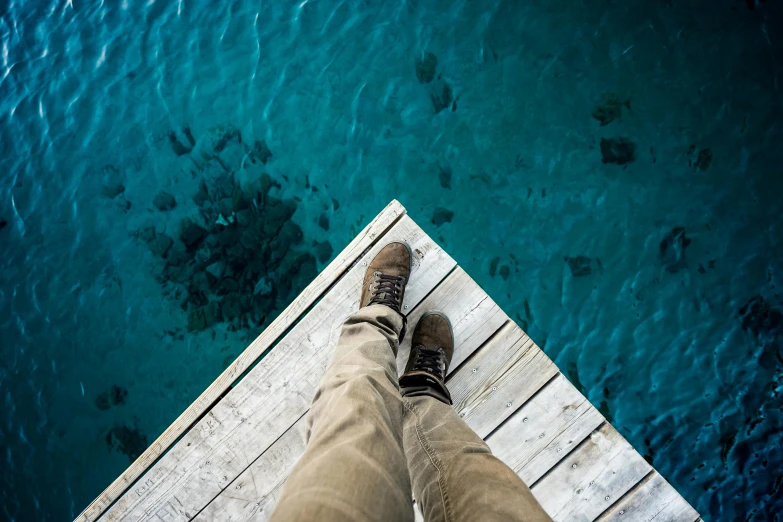 a person standing on a dock looking down at the water, pexels contest winner, high above the ground, wearing boots, clear blue water, national geographic photography