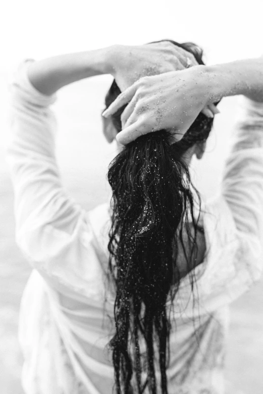 a black and white photo of a woman with long hair, by Lucia Peka, unsplash, washing her dark long hair, covered in oil, hands behind back, photo of a woman