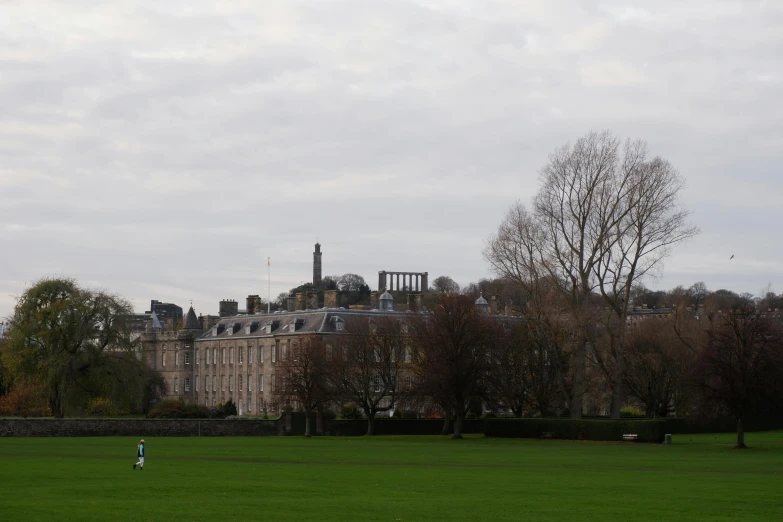 a large building sitting on top of a lush green field, by Gawen Hamilton, pexels contest winner, paris school, grey skies, with a park in the back ground, walking to the right, paisley