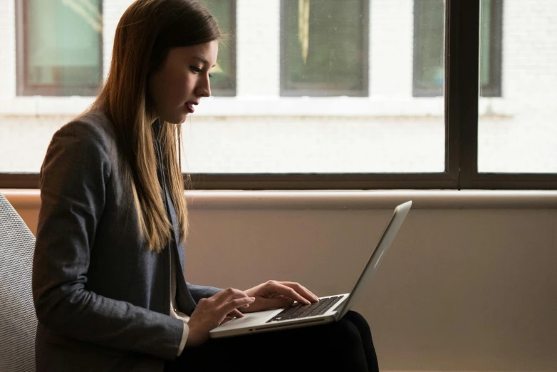 a woman sitting on a couch using a laptop, by Carey Morris, pexels contest winner, worksafe. instagram photo, female in office dress, profile image, looking serious