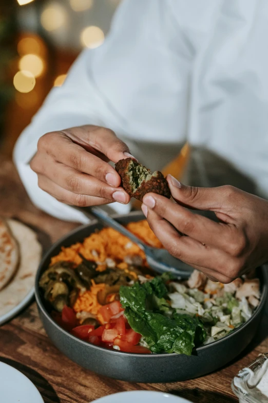 a person sitting at a table with a plate of food, hand holding a knife