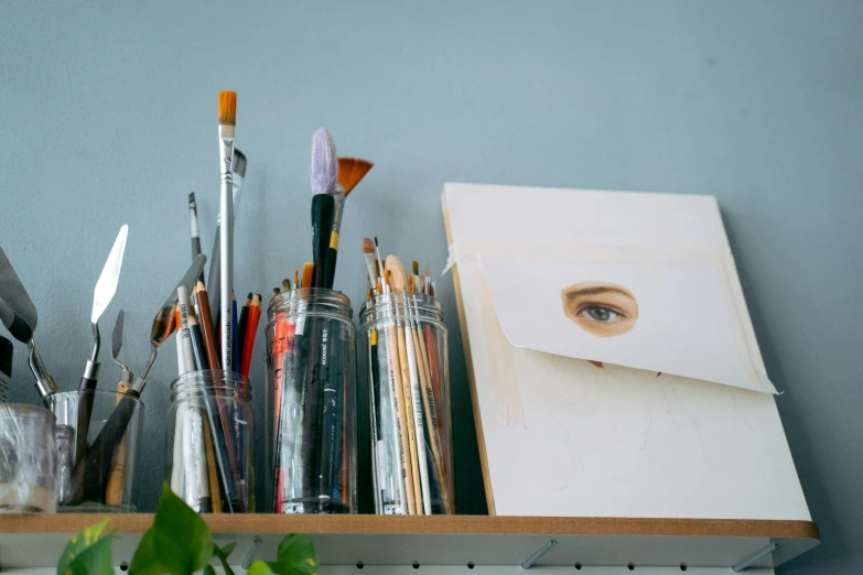 a bunch of art supplies sitting on top of a shelf, a photorealistic painting, trending on pexels, pointed face, white wall coloured workshop, looking across the shoulder, delicate and precise brushwork