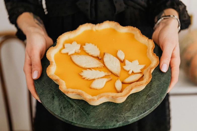 a person holding a pie with leaves on it, a still life, inspired by Elsa Beskow, trending on pexels, art nouveau, caramel, carved, flan, cut out