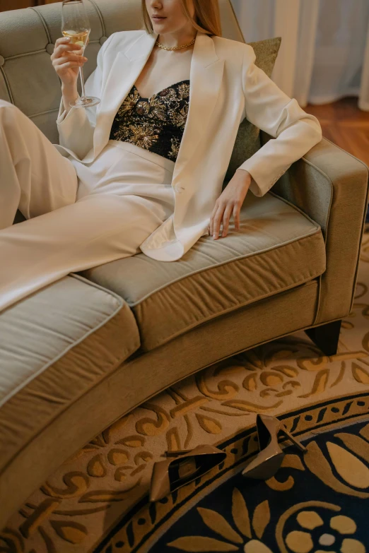 a woman sitting on a couch holding a glass of wine, inspired by Ramon Pichot, baroque, white suit and black tie, bay window sofa, ao dai, embroidered velvet