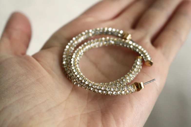 a close up of a person holding a bracelet, gold hoop earings, covered in crystals and glitter, three fourths view, thumbnail