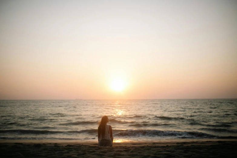 a woman standing on top of a beach next to the ocean, pexels contest winner, romanticism, watching the sunset, kneeling, profile image, sitting at the beach