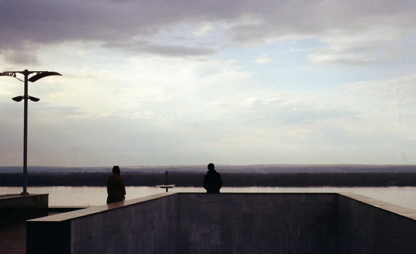 a man riding a skateboard up the side of a ramp, by Pablo Rey, minimalism, girl sitting on a rooftop, two figures, near a lake, szekely bertalan. atmospheric