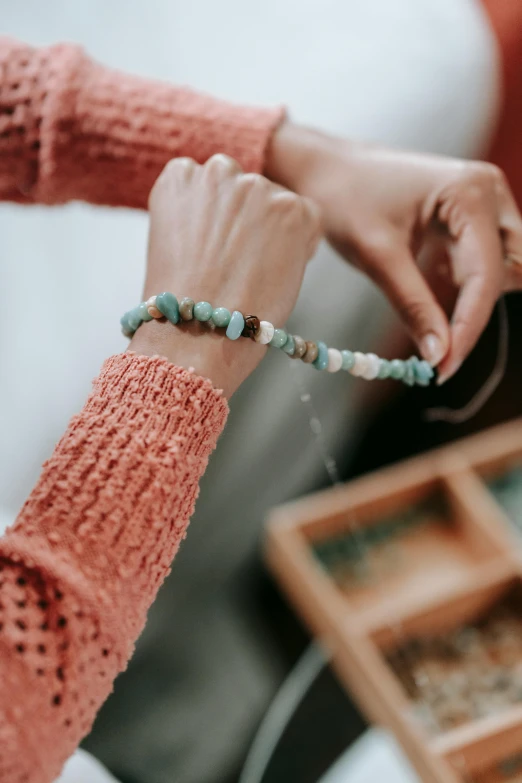 a close up of a person holding a beaded bracelet, by Robbie Trevino, mint, opal, cardboard, comforting