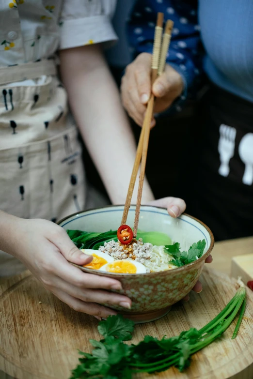 a person holding chopsticks over a bowl of food, in a kitchen, square, green, hoang lap