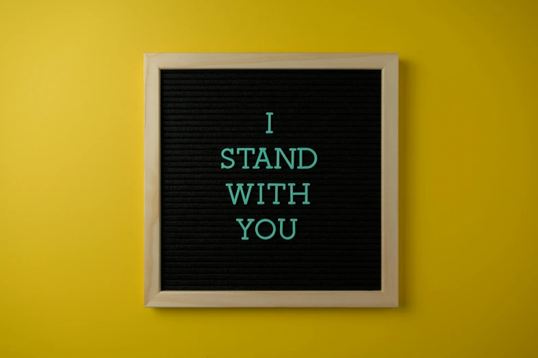 a sign that says i stand with you against a yellow wall, inspired by Carrie Mae Weems, unsplash, detailed product image, ffffound, 15081959 21121991 01012000 4k, art stand