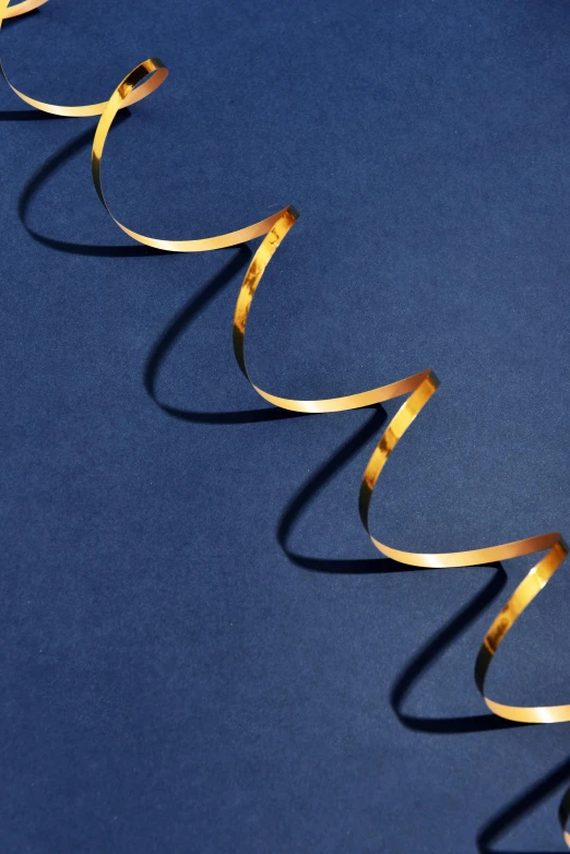 a spiral of gold ribbon on a blue surface, detailed product shot, ultra fine inklines, sustainable materials, on high-quality paper