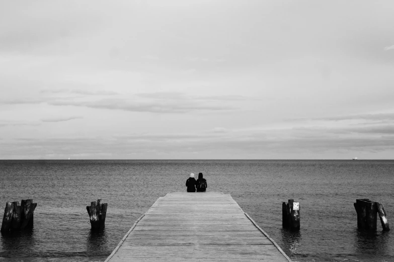 a black and white photo of two people sitting on a dock, a black and white photo, unsplash, minimalism, black sea, romantic couple, sittin