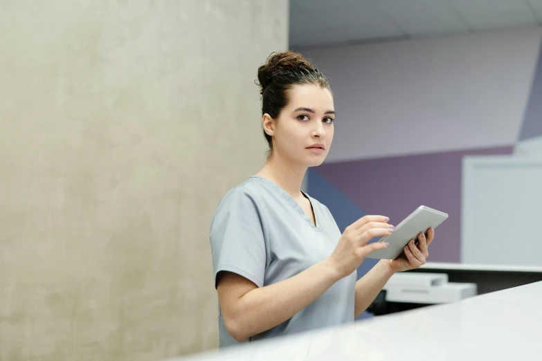 a woman in scrubs using a tablet computer, unsplash, standing sideways, greys, charli bowater, aged 2 5