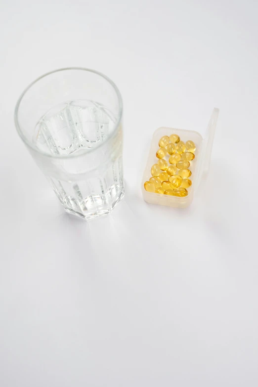 a glass of water and a pill on a table, bolts of bright yellow fish, set against a white background, 2 people, product image