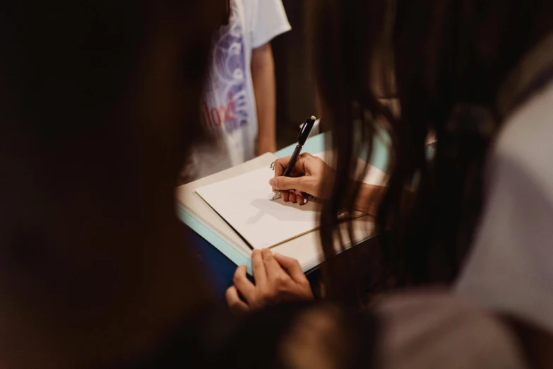 a close up of a person writing on a piece of paper, a group of people, background image, taken in the early 2020s, an escape room in a small