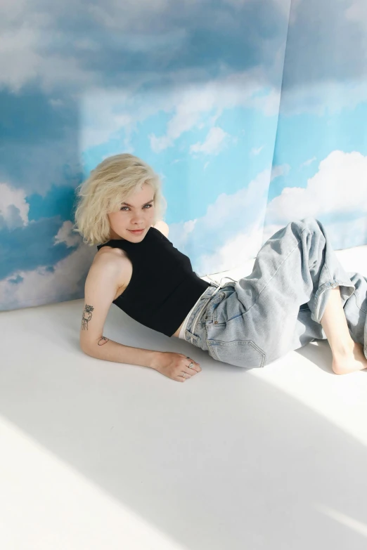a woman laying on top of a white floor next to a wall, an album cover, inspired by Elsa Bleda, trending on pexels, short platinum hair tomboy, standing on a cloud, ivory pale skin, baggy jeans