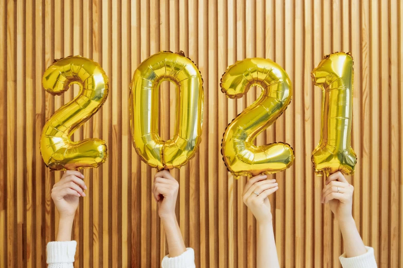 a group of people holding up balloons that say 2021, by Julia Pishtar, trending on pexels, shades of gold display naturally, glossy yellow, reverse, diy