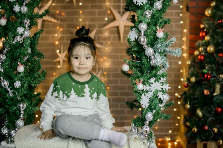 a little girl sitting on a blanket in front of a christmas tree, pexels contest winner, hurufiyya, green and white, young asian girl, avatar image, a handsome