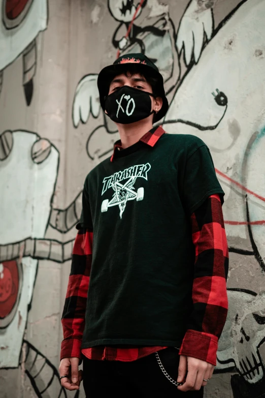 a man standing in front of a graffiti covered wall, inspired by Yi Insang, graffiti, lumberjack flannel, wearing all black mempo mask, x logo, band merchandise