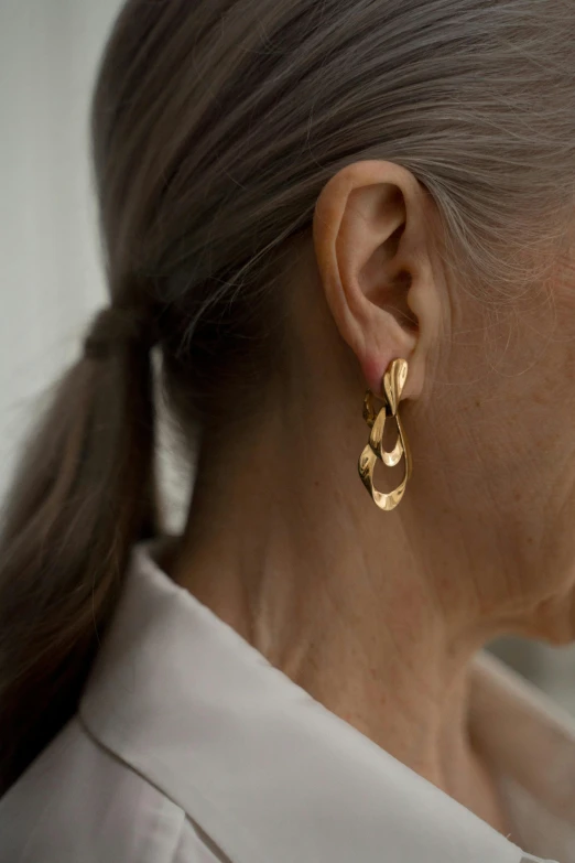 a close up of a person wearing a pair of earrings, inspired by Caro Niederer, liquid gold, 7 0 years old, multiple levels, sleek flowing shapes