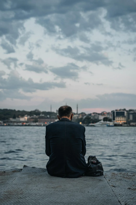 a man in a suit sitting on the edge of a pier, by irakli nadar, istanbul, unsplash photography, thoughtful, sittin