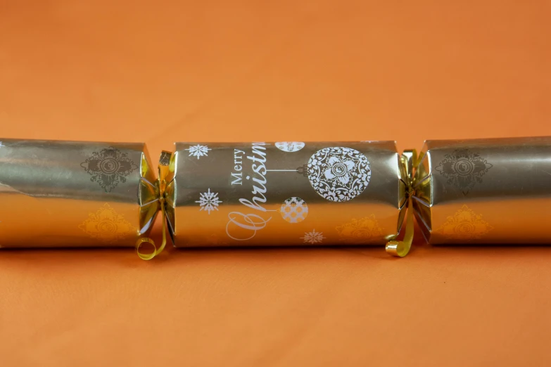 a couple of rolls of chocolate sitting on top of a table, silver with gold trim, high quality product image”, with an explosion on the back, christmas