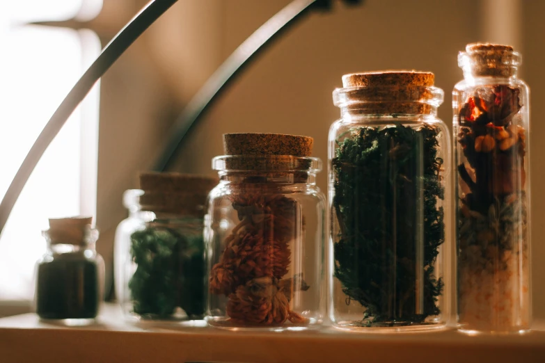 a shelf filled with bottles filled with different types of herbs, trending on pexels, visual art, inside a glass jar, jewelry, early evening, in a row