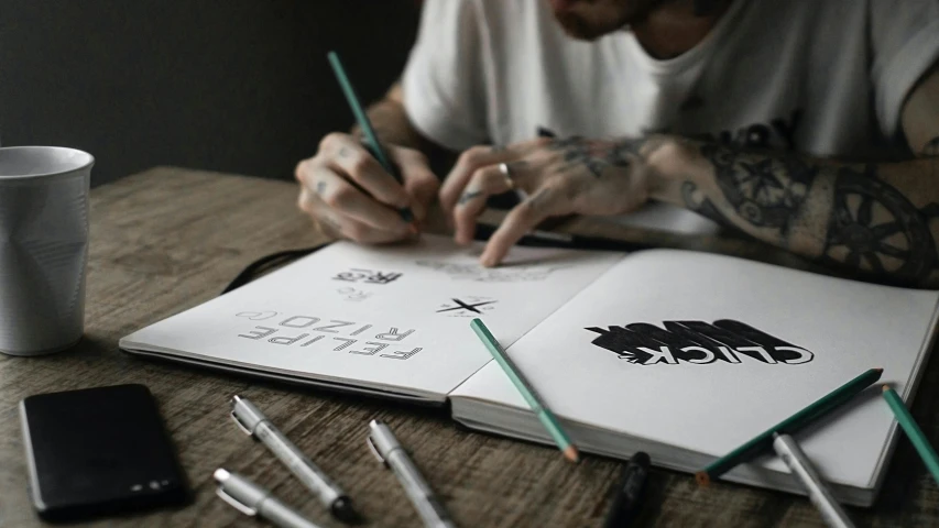 a man sitting at a table writing on a notebook, a drawing, by Adam Marczyński, pexels contest winner, process art, tattoo stencil, logotype design, 9 9 designs, drawing an arrow from his quiver