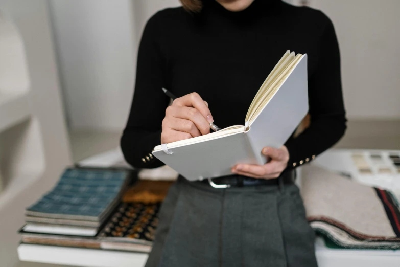 a woman holding a pen and writing in a book, private press, white shirt and grey skirt, curated collections, thumbnail, thick lining