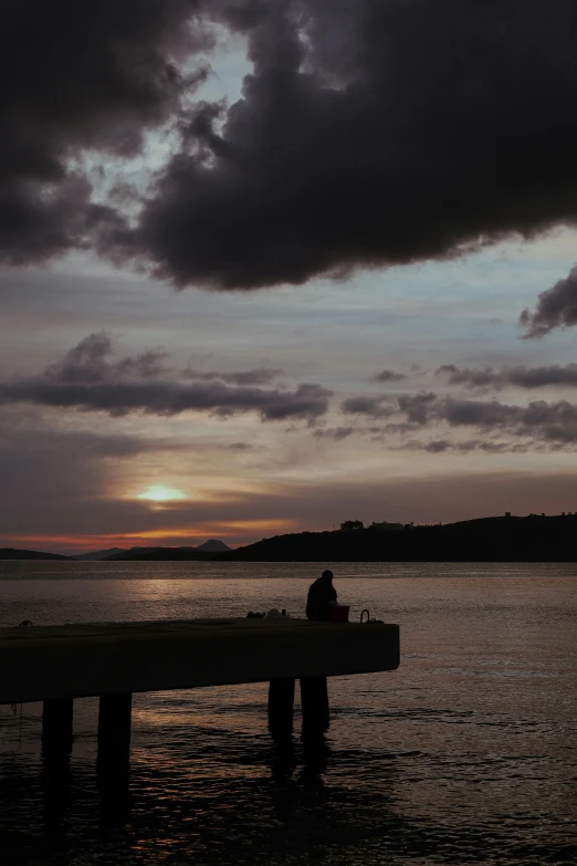 a couple of people sitting on top of a wooden pier, unsplash, romanticism, overcast dusk, skye meaker, silhouette of a man, sittin