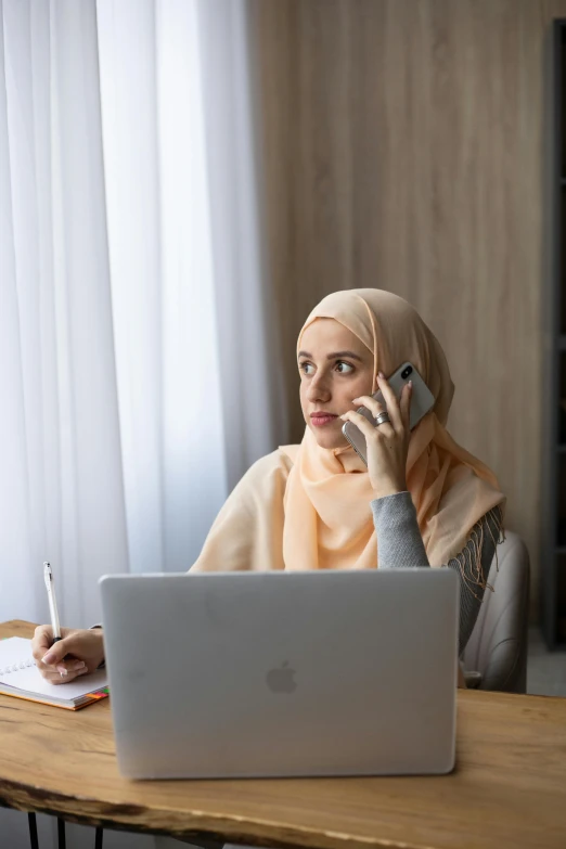 a woman sitting at a table talking on a cell phone, inspired by Maryam Hashemi, trending on pexels, hurufiyya, sitting at a computer, serious expression, malaysian, ( ( theatrical ) )