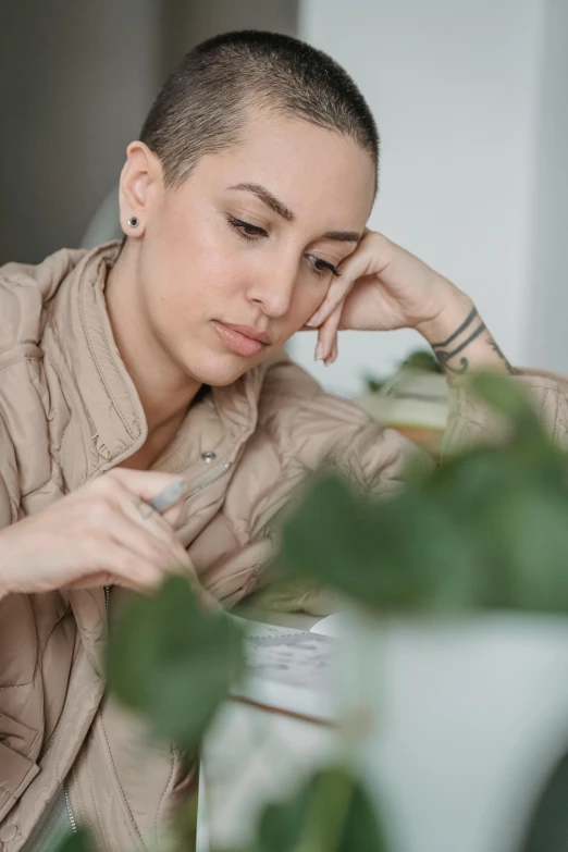 a woman sitting at a table with a cup of coffee, brown buzzcut, next to a plant, stressed out, concentrated