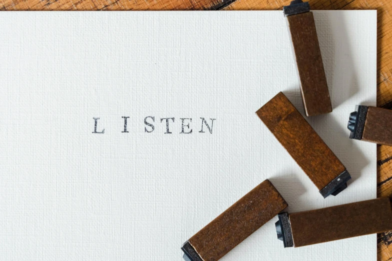 a piece of paper sitting on top of a wooden table, an album cover, inspired by Wilhelm Hammershøi, unsplash, letterism, ears are listening, linen canvas, lie detector test, sittin