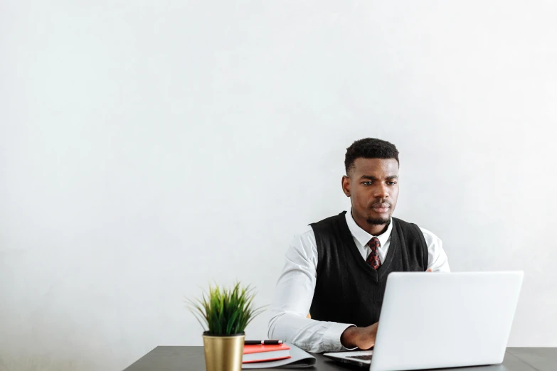 a man sitting at a desk using a laptop computer, trending on pexels, wearing a vest and a tie, black man, white space in middle, studious