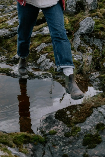 a woman standing on top of a rock next to a puddle of water, doc marten boots, walking towards camera, standing on a shelf, explore