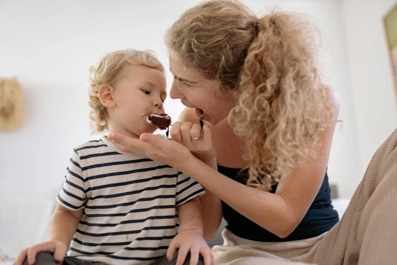 a woman feeding a child a piece of chocolate, by Emma Andijewska, pexels contest winner, avatar image, handsome, manuka, 1 4 9 3