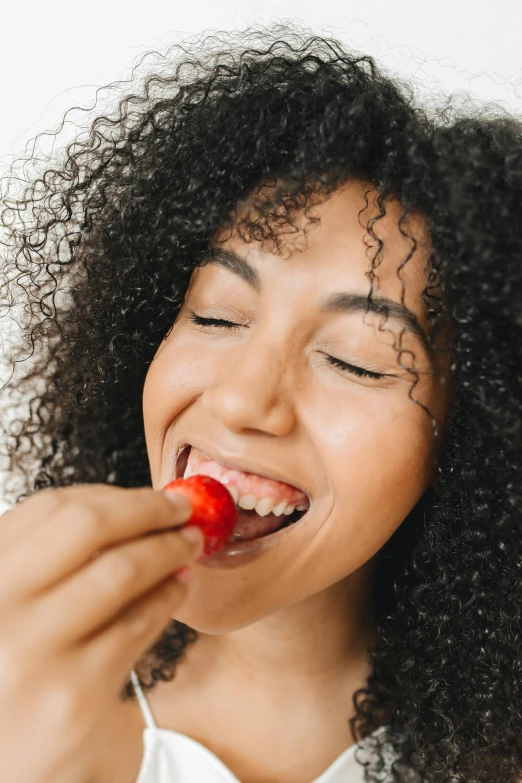 a close up of a person eating a strawberry, she is smiling, wavy hair spread out, natural complexion, candy treatments