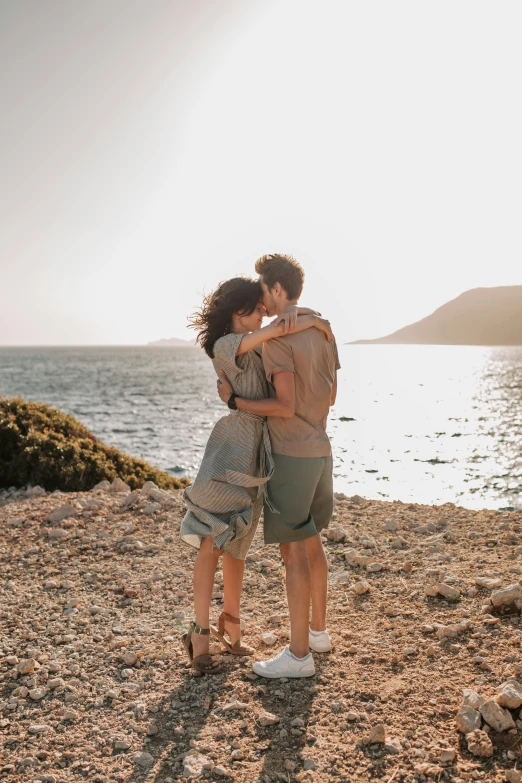 a couple standing next to each other on a beach, by Alexis Grimou, pexels contest winner, loving embrace, on an island, instagram post, greece