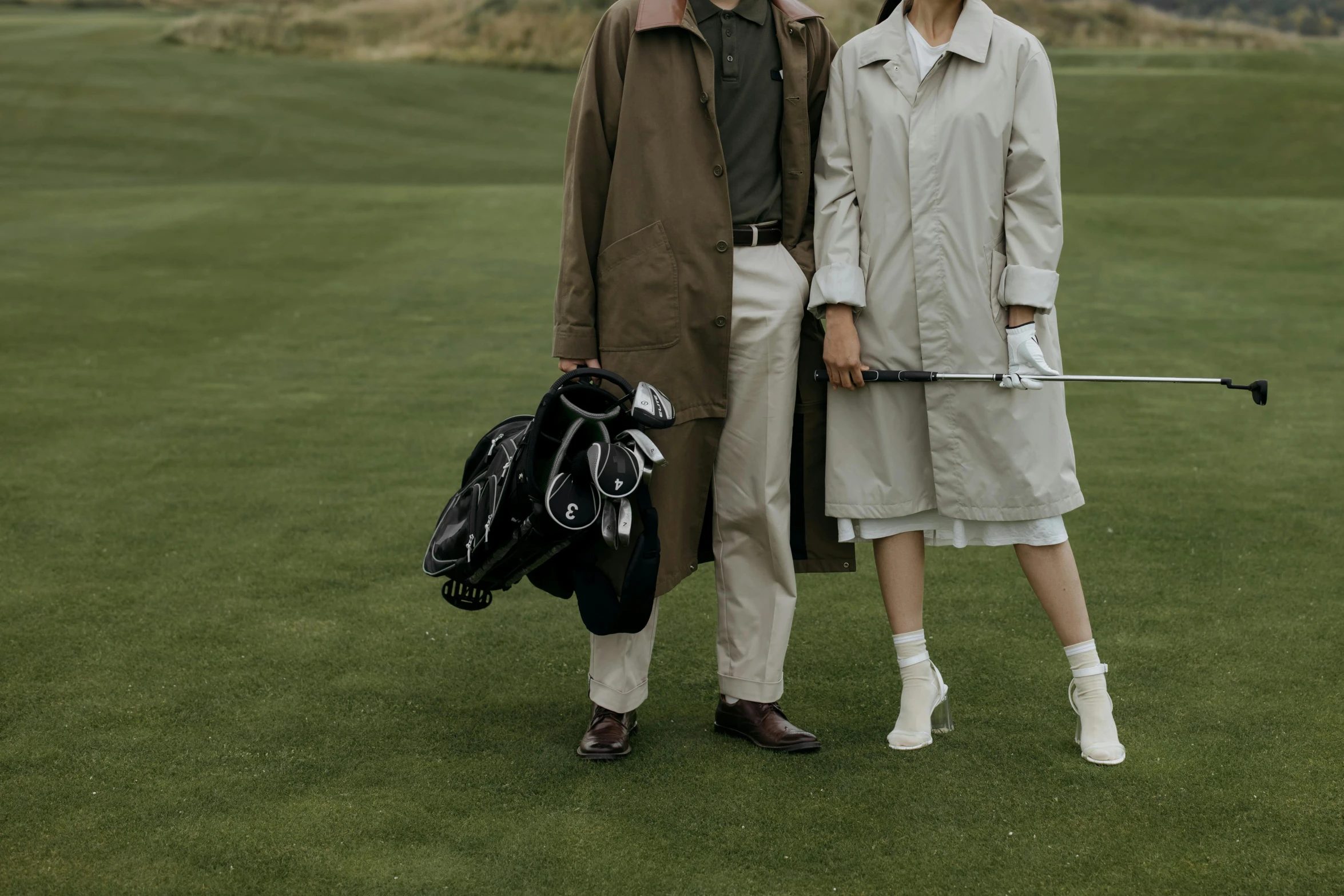 a man and woman standing next to each other on a golf course, pexels contest winner, renaissance, trench coat, bags on ground, gemma chen, plain background