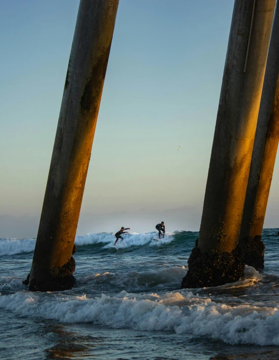 a person riding a surfboard under a pier, high towers, in the ocean