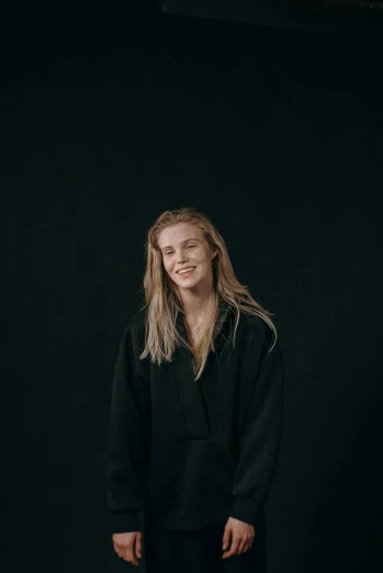 a woman standing in front of a black background, by Sara Saftleven, nina agdal, wearing an academic gown, wearing a black shirt, kieth thomsen