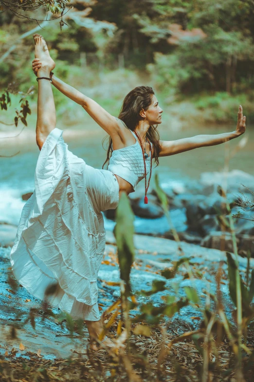 a woman doing a yoga pose in front of a river, arabesque, tribal clothing, amidst nature, profile image, feature